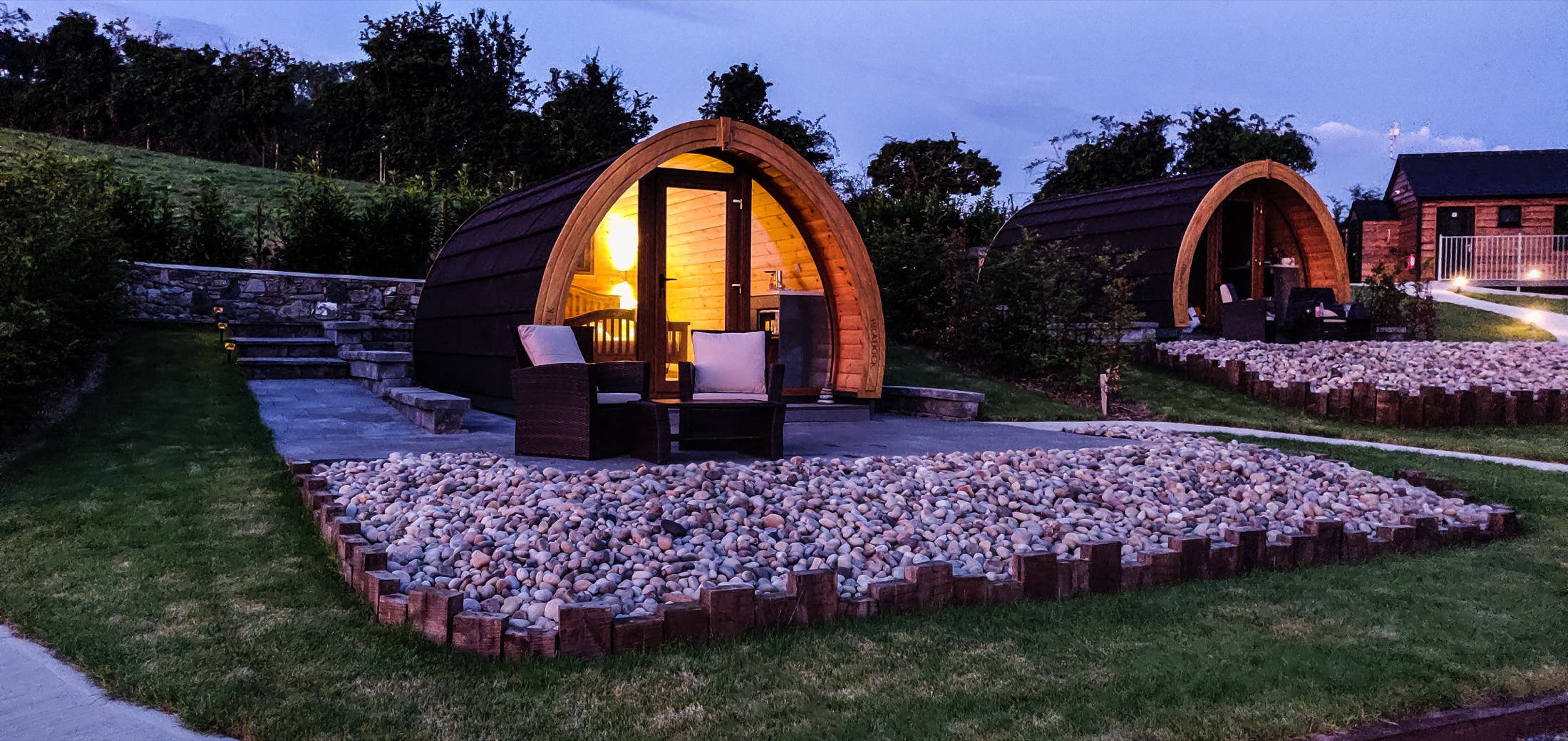 Warmly lit pod at dusk with outdoor seating and a stone terrace